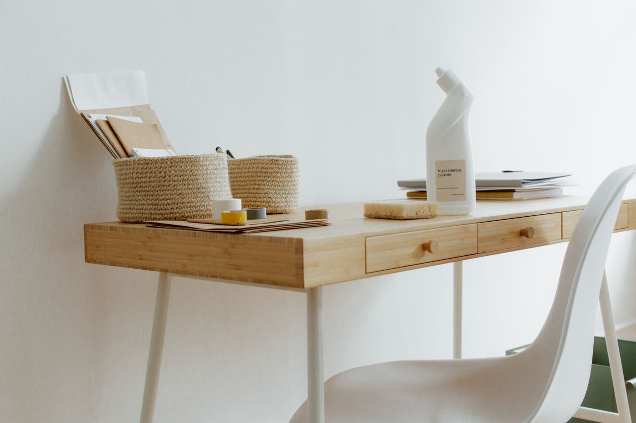 A tidy, well-arranged home office desk with cleaning supplies, documents, and storage baskets.